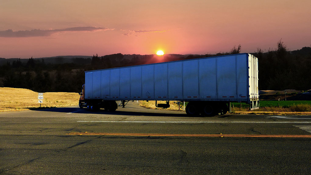 Texas Top Notch Trucking white cargo truck turning down a road into a beautiful sunrise